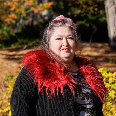 A headshot of Heather. She wears a black coat with red frills.