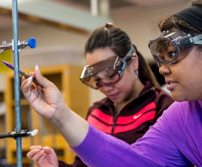 Two students wear goggles and examine a measuring instrument