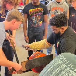 An artist works on a piece of glass art with several students