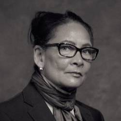 A black and white headshot of an artist wearing glasses with her hair pulled back