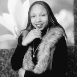 A black and white headshot of an artist wearing a fur vest