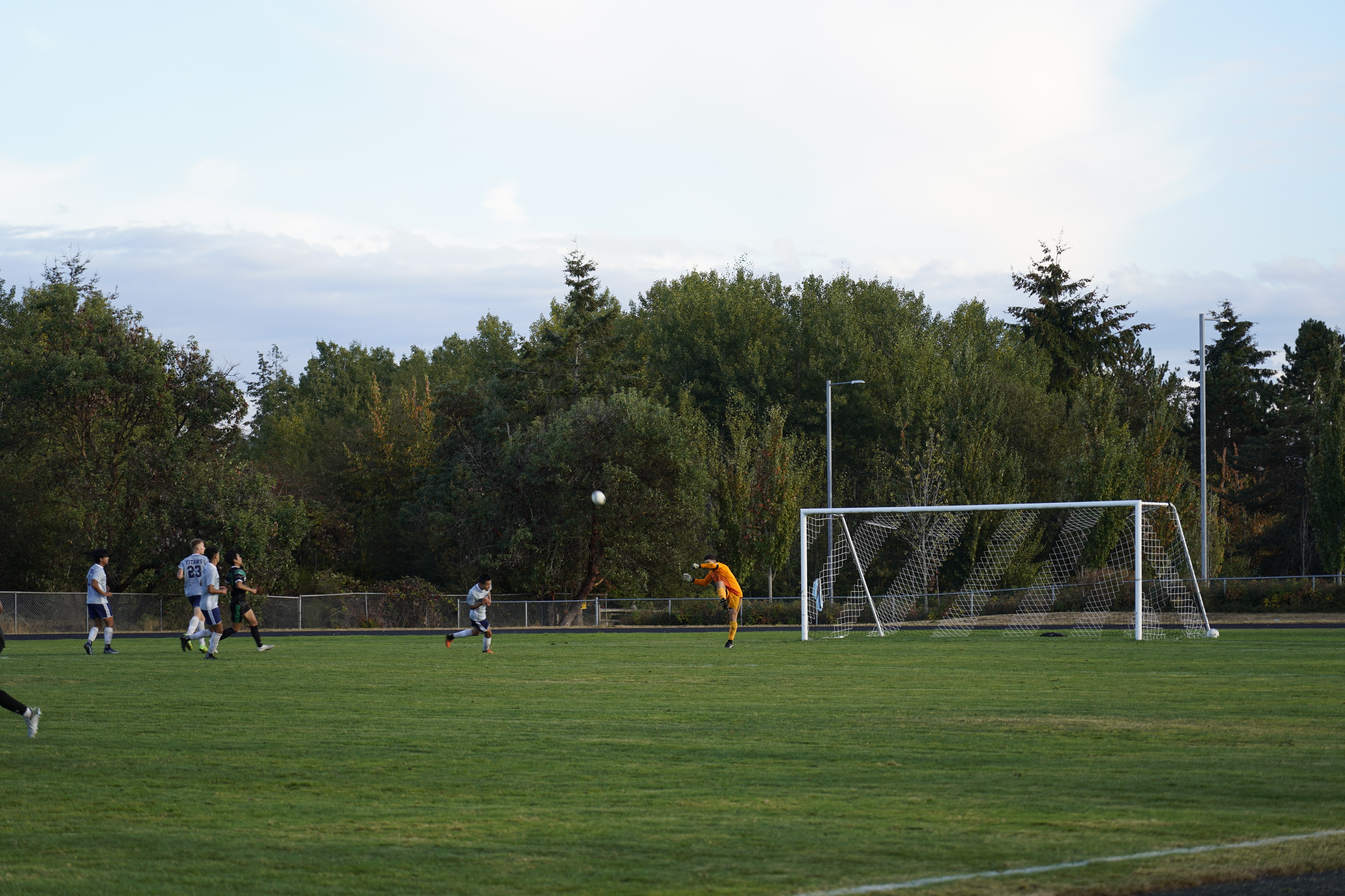 a wide shot of soccer field, showcasing green grass and a student defending the goal from a soccer ball