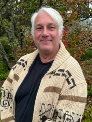 An image of a white man in a tan and black sweater