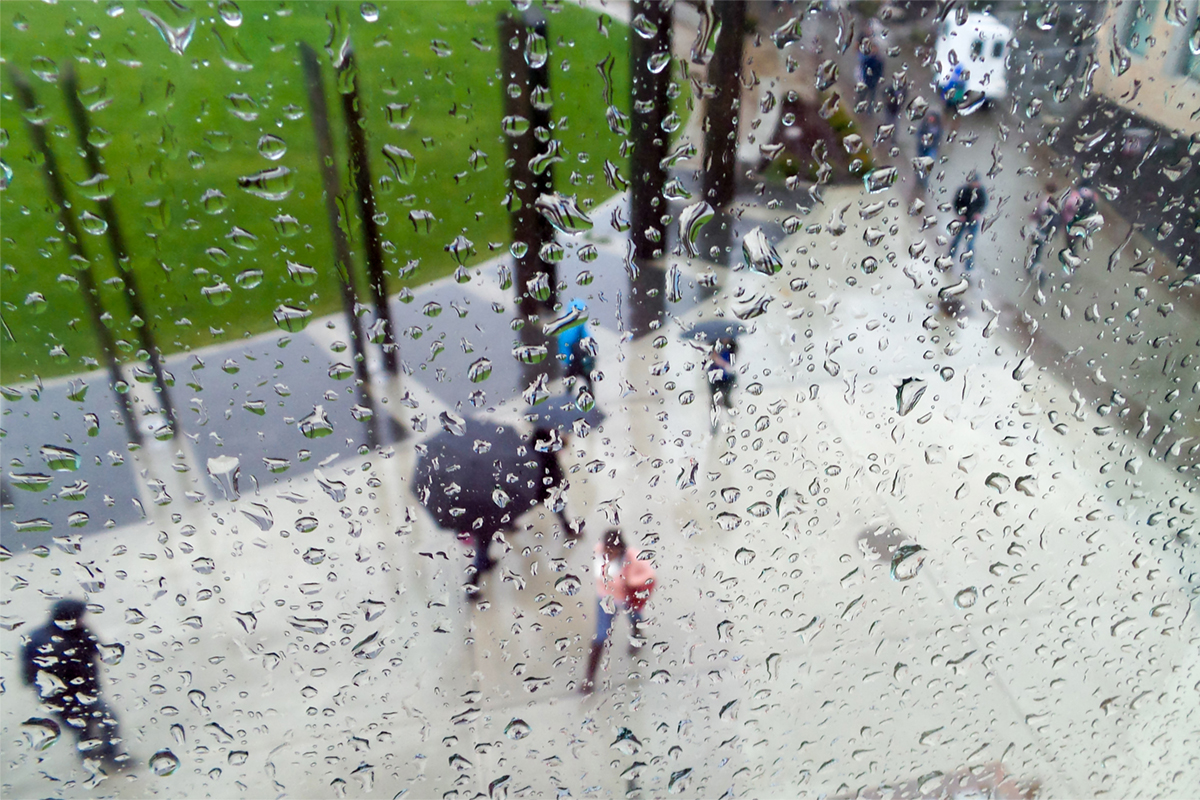 Aerial view through a rainwashed window of students walking across the Trustee Plaza, some with umbrellas