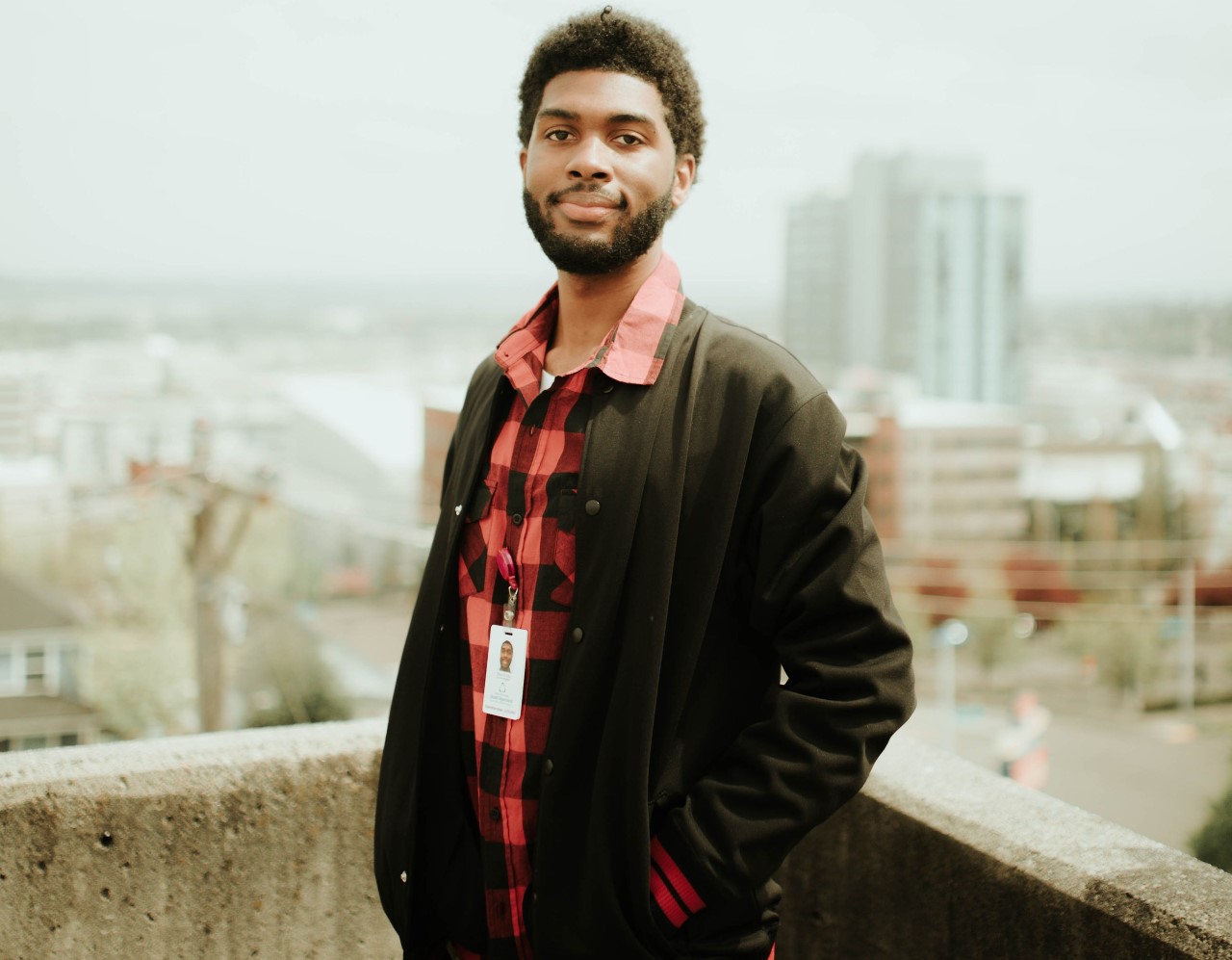 student wearing a red flannel and black jacket poses against a city skyline 