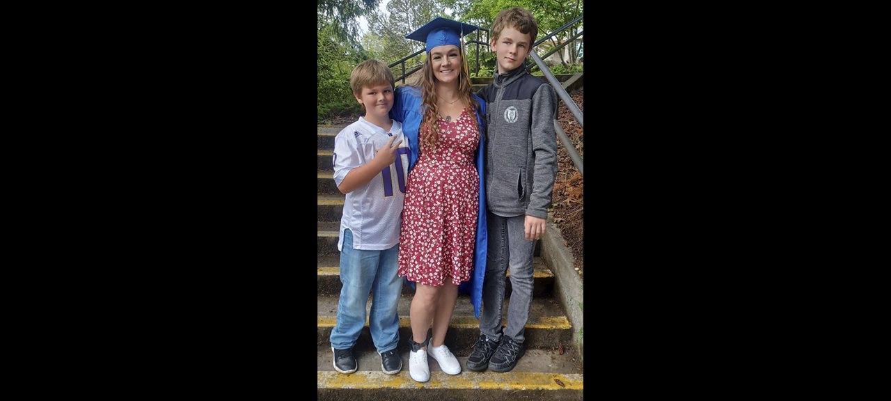  student in grad regalia poses with two young boys