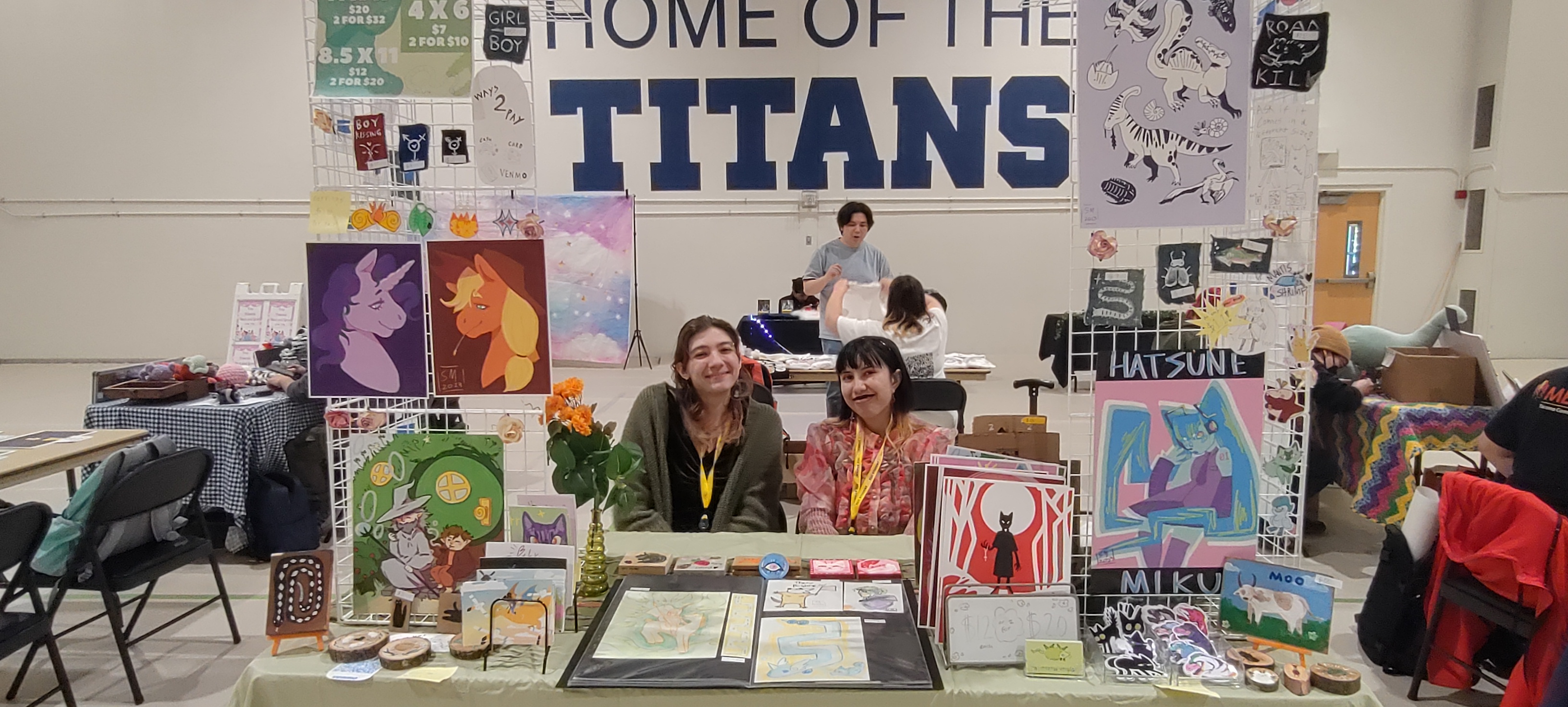 Photo of two people at a table with art, "Home of the Titans" on the wall in the background. 