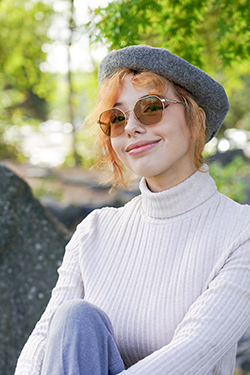 Photo of a woman with red hair wearing tinted glasses, a white sweater, and a grey beret. 