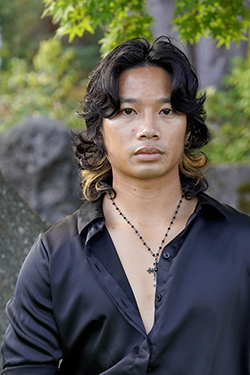 Picture of a man wearing a black shirt and a cross necklace. 