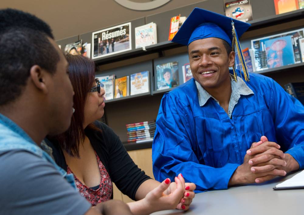 A student in graduation regalia sits at the career center with a career counselor