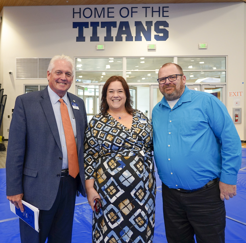 A woman and two men smiling under a sign that says home of the Titans