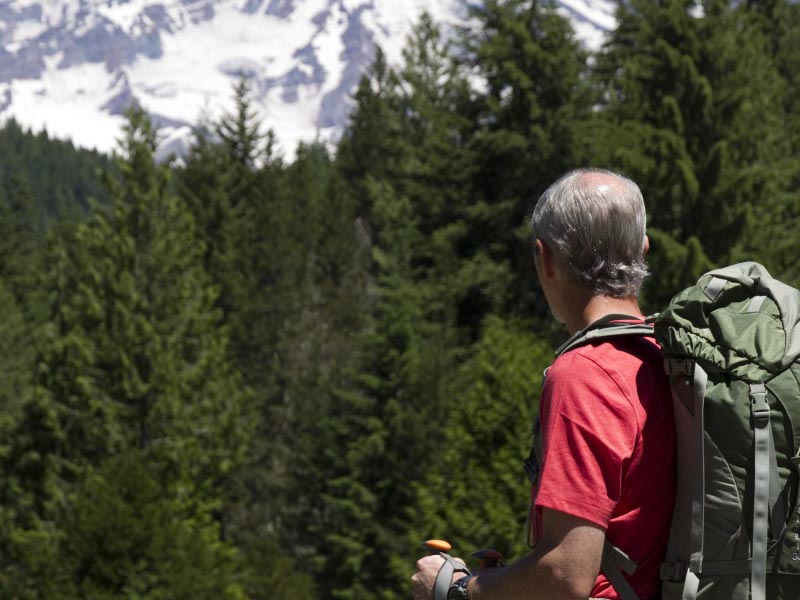 A man with a backpack standing on a trail looking towards Mount Rainier